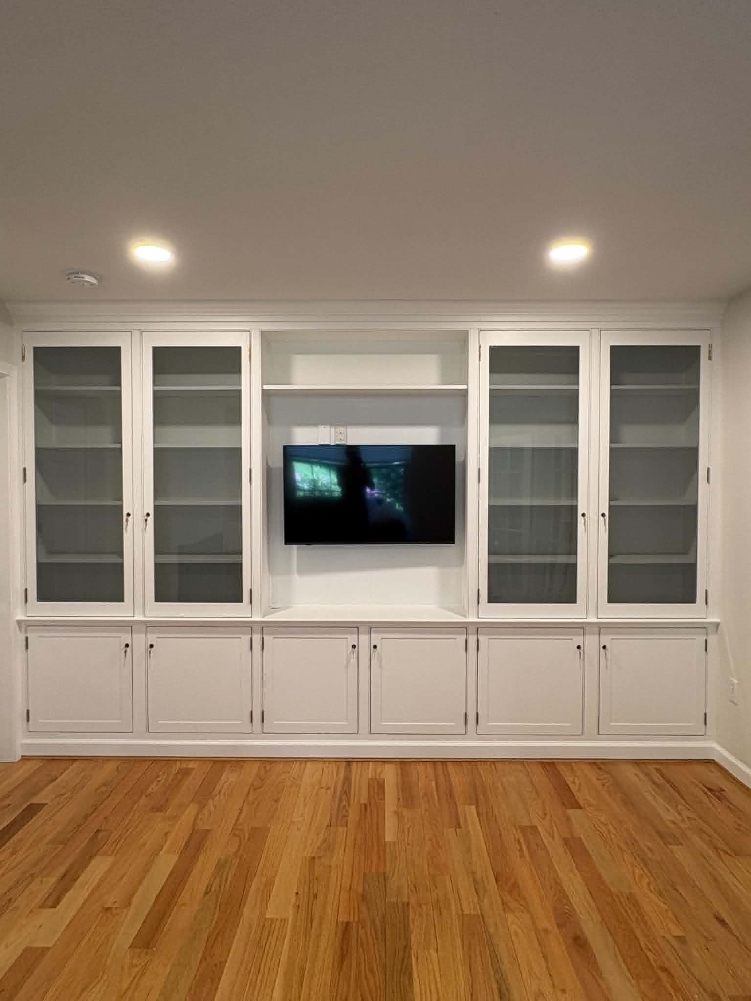 Built-in entertainment center finished and installed — glass doors, center TV niche, white finish