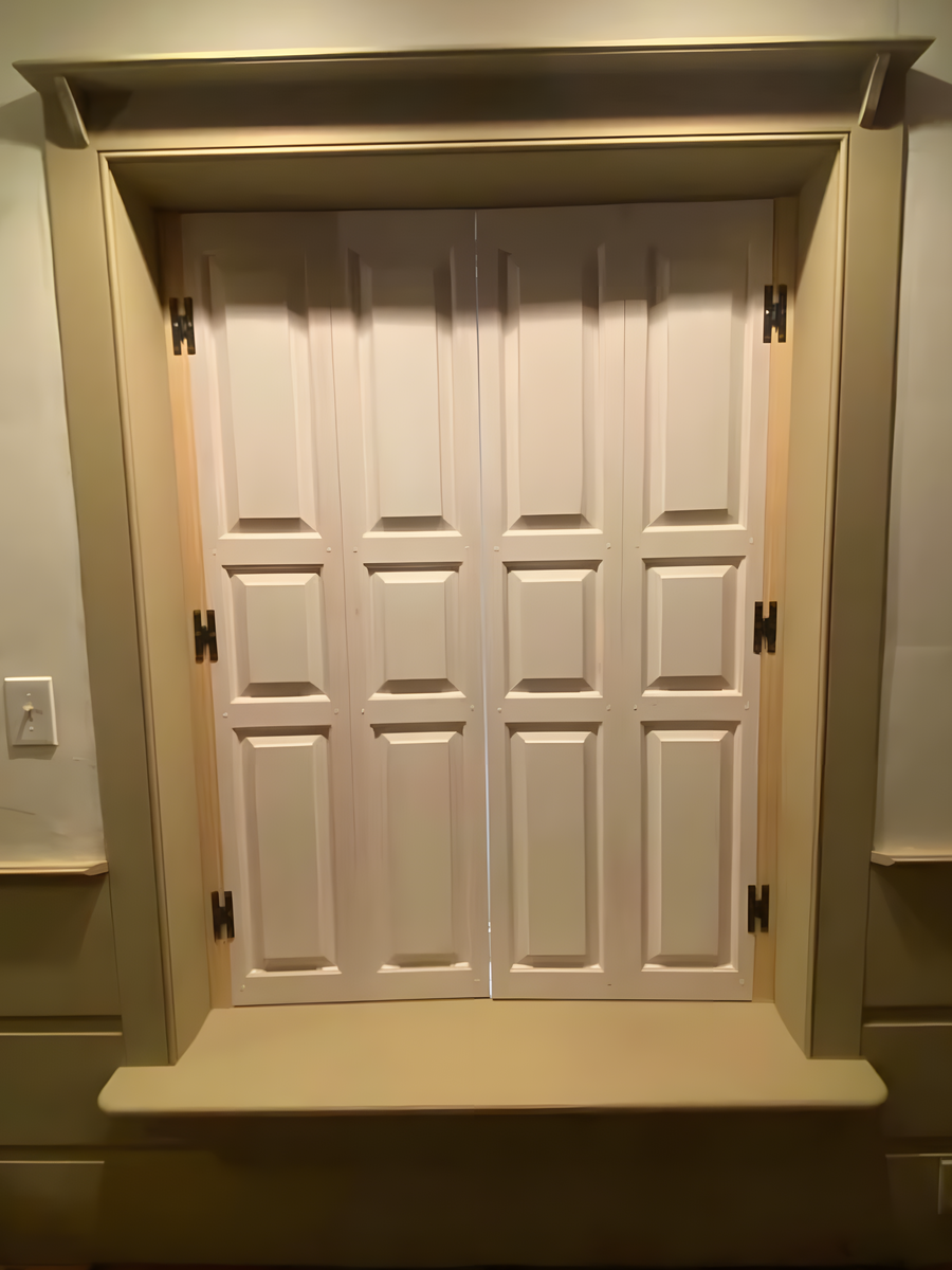 Installed raised-panel interior window shutters folded open, cream painted finish