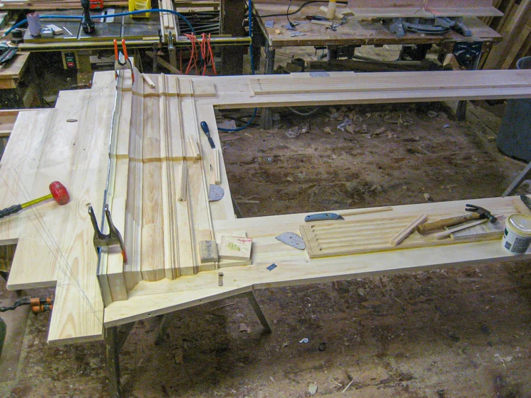 Pediment cornice pieces laid out in raw pine, wide shop view