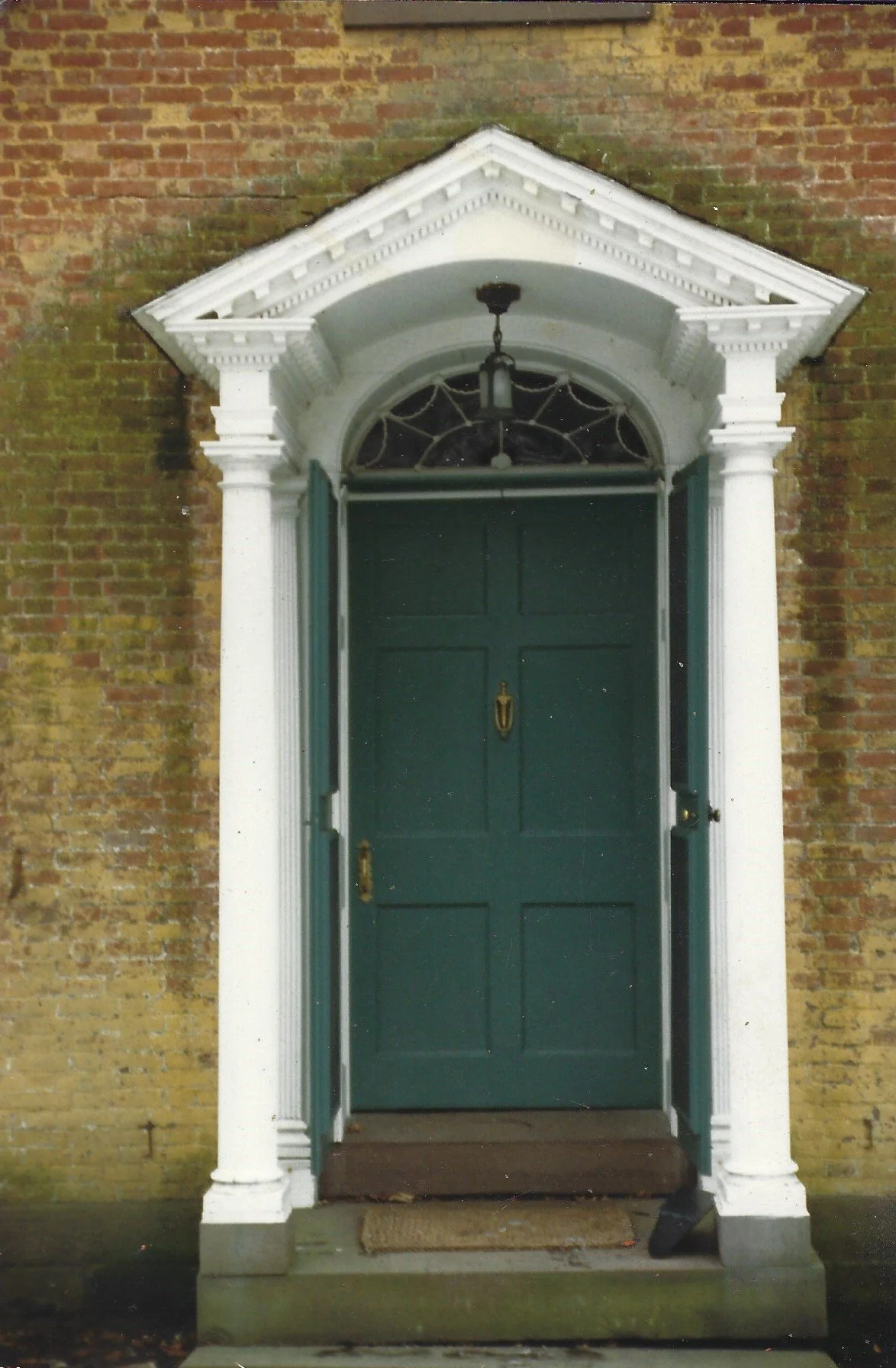 Arched pediment entryway with green door and white columns, installed exterior