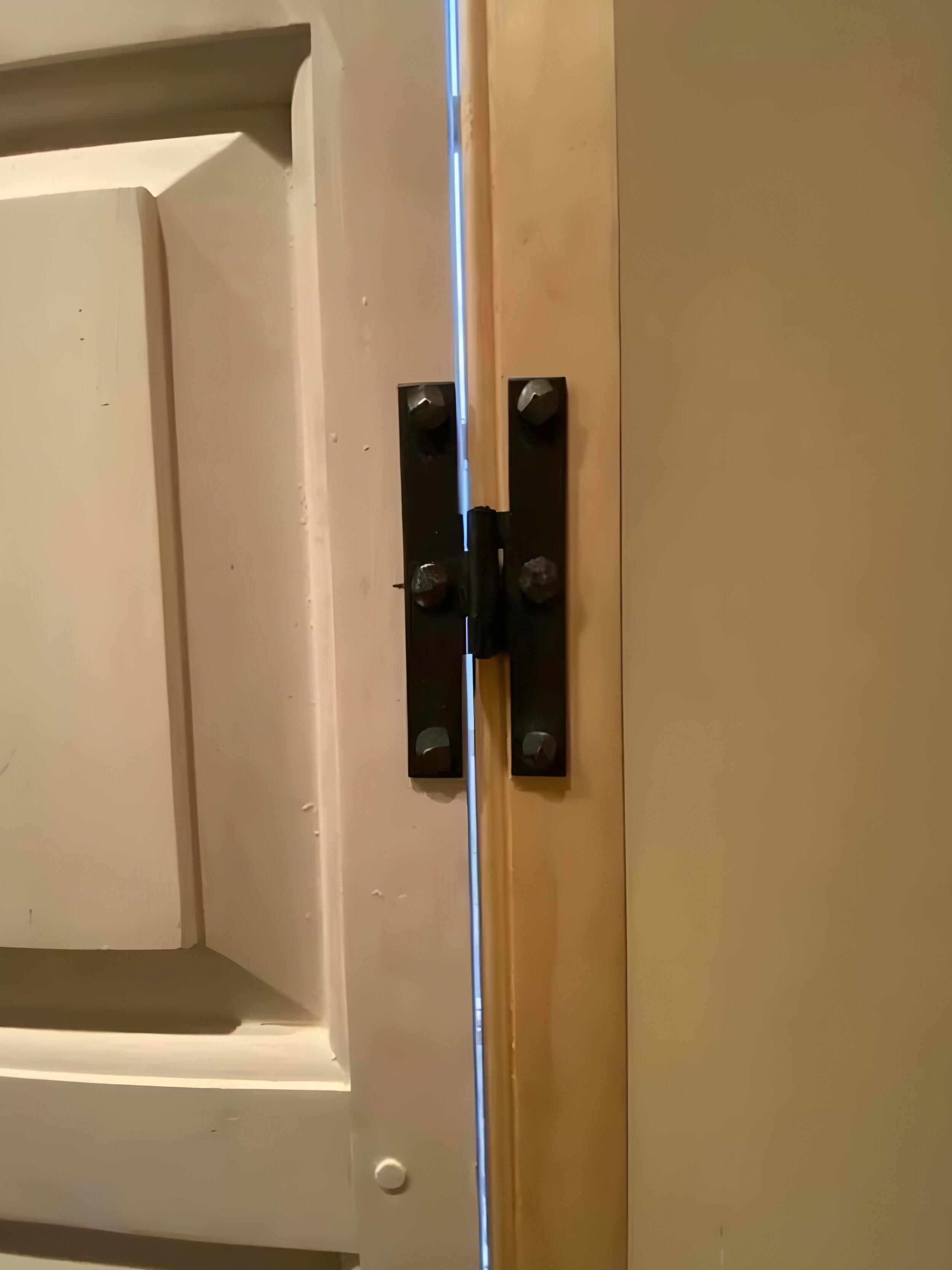 Black H-hinge close-up on white shutter panel against natural wood stile