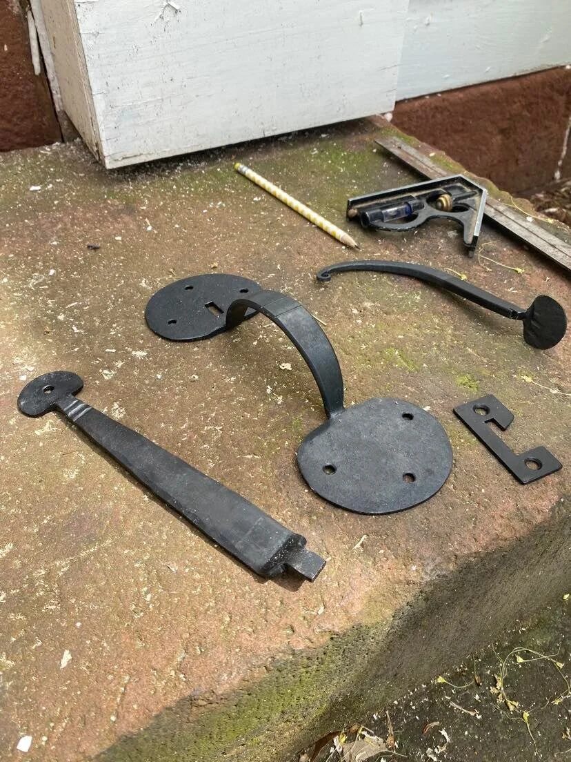 Period-style black cast iron door handle, hinge plates, and hardware components laid out on stone step