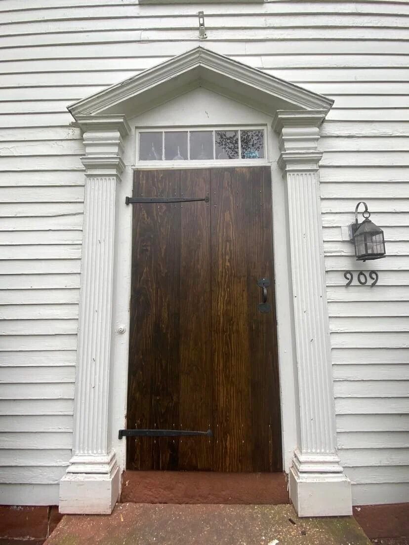 Storm door installed in triangular pediment entryway surround on white colonial exterior, house number 909
