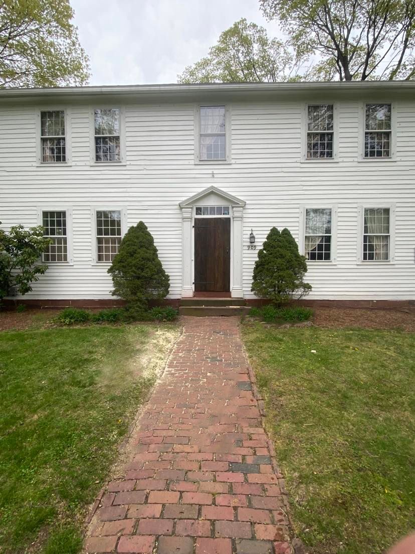 Wide exterior view of white colonial home 909 with completed storm door installation and brick walkway