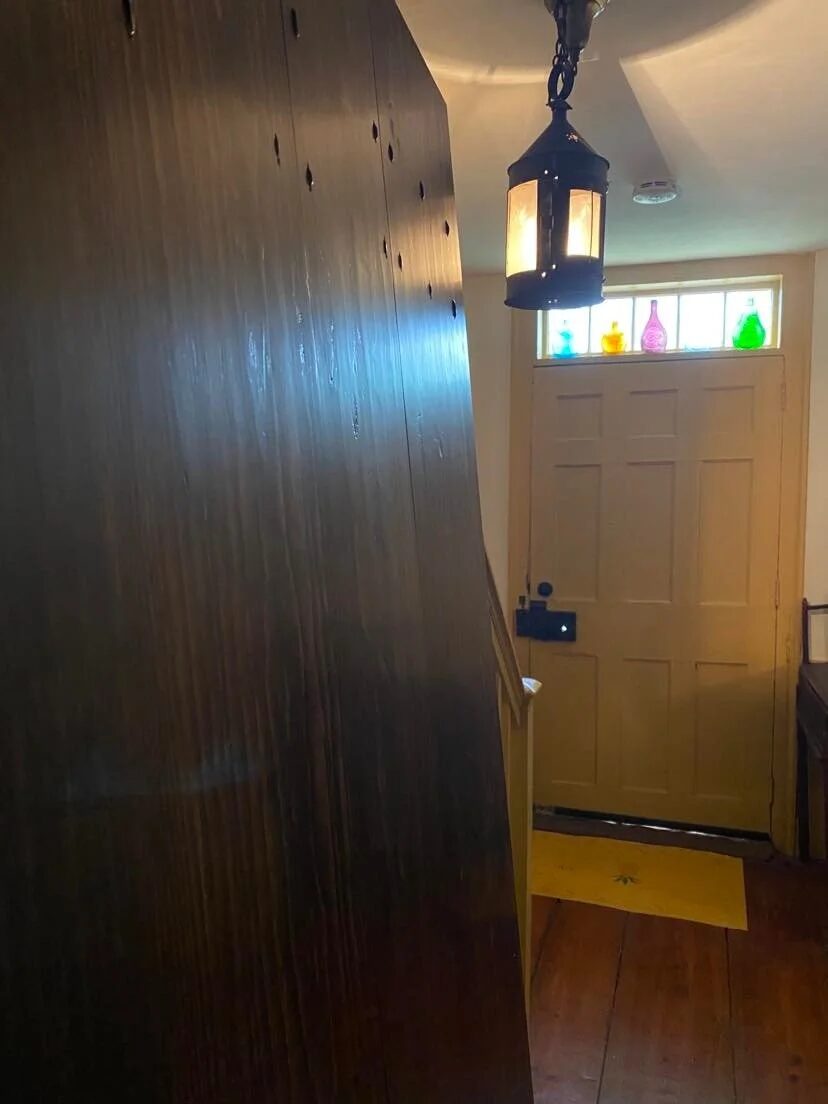 Installed storm door open from interior showing entryway hall with period lantern overhead and colored glass transom