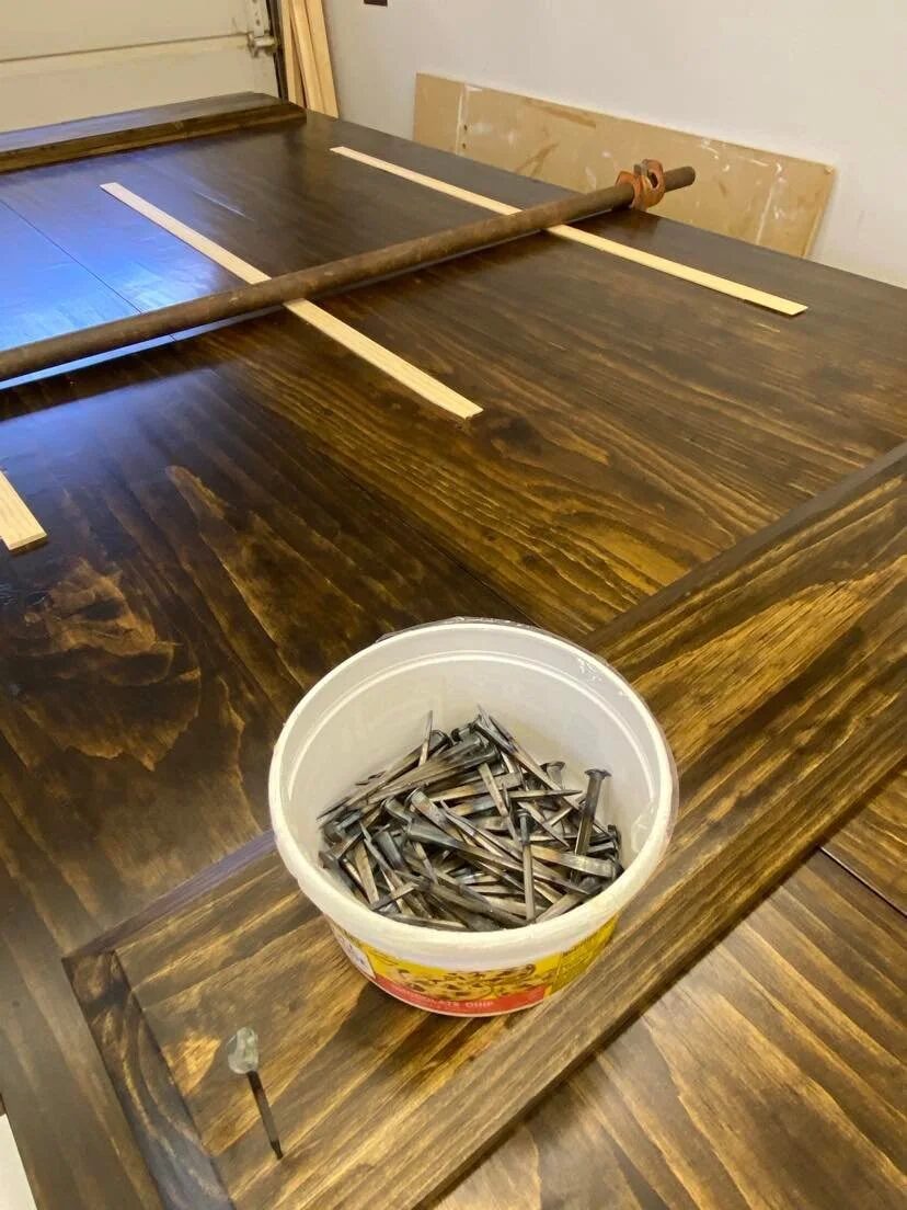 Storm door panels laid flat on workbench with cut nails in a bucket during assembly