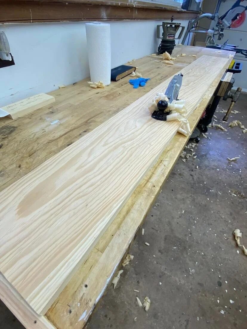 Raw pine boards planed smooth on long workbench during storm door fabrication